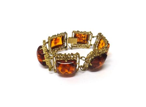 A reconstituted amber panel link bracelet, each shaped rectangular link decorated with a cast and pierced border, in an abstract design, on a snap cla