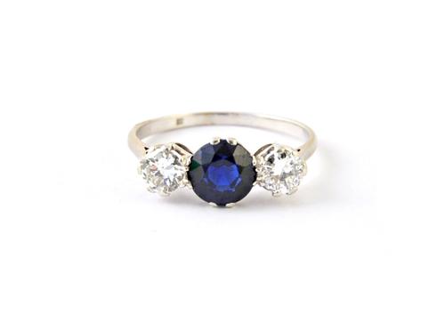 A platinum, diamond and sapphire set three stone ring, claw set with the circular cut sapphire at the centre, between two circular cut diamonds, ring