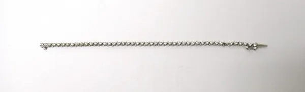 A white gold and diamond set line bracelet, claw set with a row of circular cut diamonds, on a snap clasp, with a foldover safety catch (one diamond l