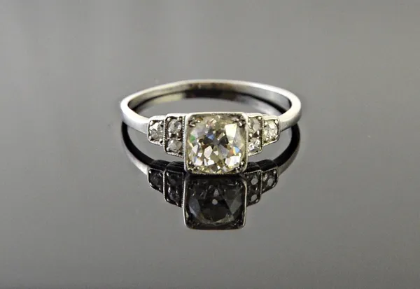 A diamond ring, mounted with the principal cushion shaped diamond at the centre, in a square shaped setting between diamond set three stone shoulders,