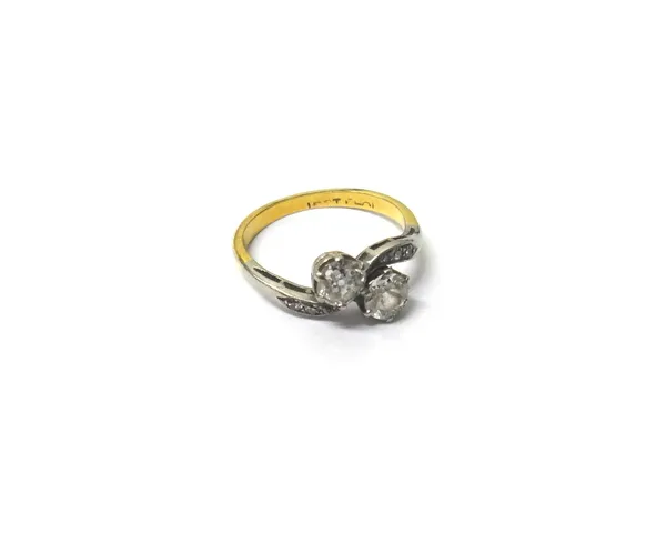 A gold and platinum, diamond set two stone ring, claw set with cushion shaped diamonds, in a crossover design, between diamond set three stone shoulde