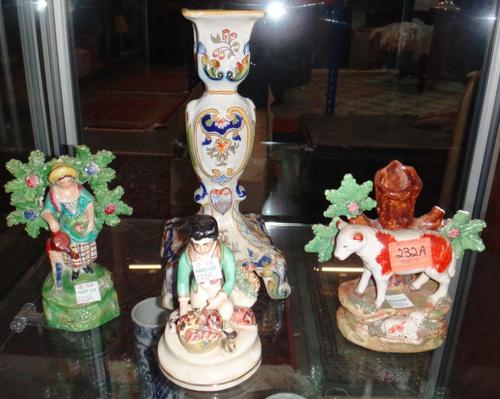 A Staffordshire flatback figure of a sheep, together with another of a gardener, another figure gathering shells and a faience pottery candle stick.