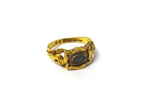 A Victorian 18ct gold mourning ring, the centre mounted with an oval glazed hair locket, within a rectangular surround, having a scrolling border, bet