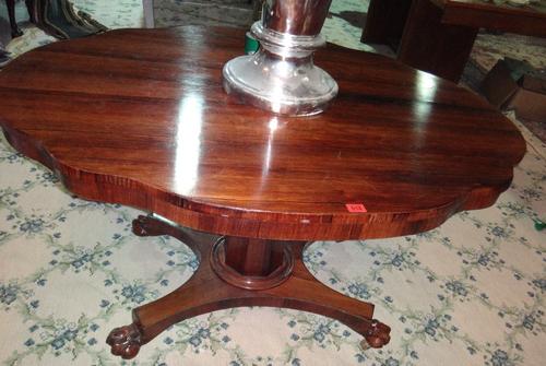 A William IV rosewood centre table, the shaped oval top on tapering octagonal column, on quatrefoil platform and lions paw feet, 130cm wide x 101cm de