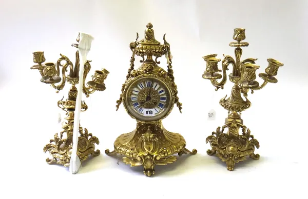 A French gilt brass mantel clock garniture of Louis XVI style, 20th century, the drum case with enamel numerals and ornately cast with applied foliate