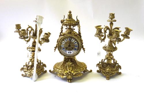 A French gilt brass mantel clock garniture of Louis XVI style, 20th century, the drum case with enamel numerals and ornately cast with applied foliate