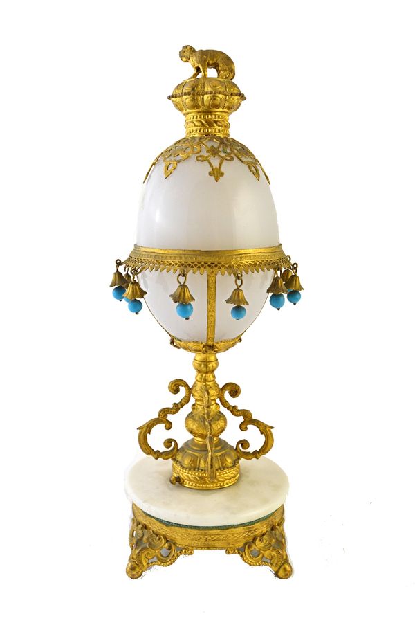 An early 20th century gilt metal and opaque glass mounted scent bottle stand of egg form, with dog finial over a tasselled cover, enclosing four ename
