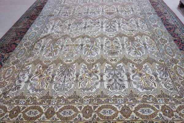 A Qum carpet, Persian, the ivory field with ovals of flowering plants, an ivory palmette and cartouche border, 346cm x 236cm.