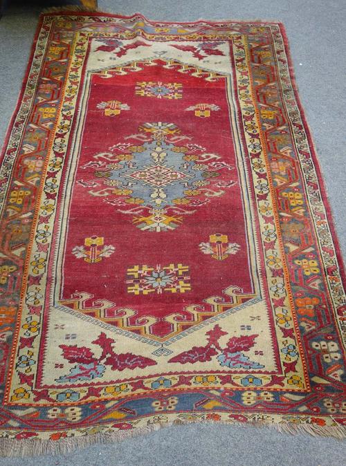 A Ghiordes rug, Darleish, the madder field with an indigo medallion, ivory ends, a grey vine and flowerhead border, 175cm x 114cm.