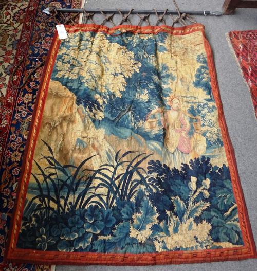 An early 18th century tapestry fragment depicting a milkmaid in rocky landscape with trees, suspended on an iron bracket with rope and tassel, 155cm x