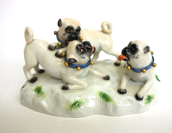 A Meissen porcelain pug group,  20th century, modelled with three playful young pugs atop a naturalistic base, underglaze blue crossed swords, incised