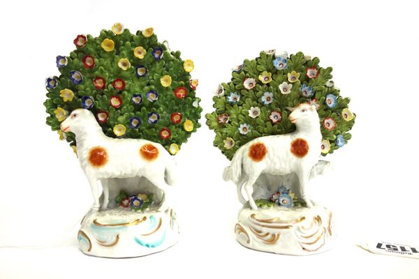 A pair of Continental Derby style porcelain sheep, early 20th century, each modelled in front of a floral bocage, 14.5cm high. (2)