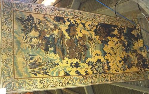 An 18th century style woven wall panel, early 20th century, depicting a landscape scene bordered by trees and birds, 300cm x 135cm.