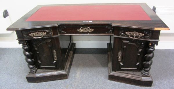 A stained carved oak Arts & Crafts pedestal desk, the inverted break front top over three frieze drawers and a pair of cupboards, with barleytwist mou