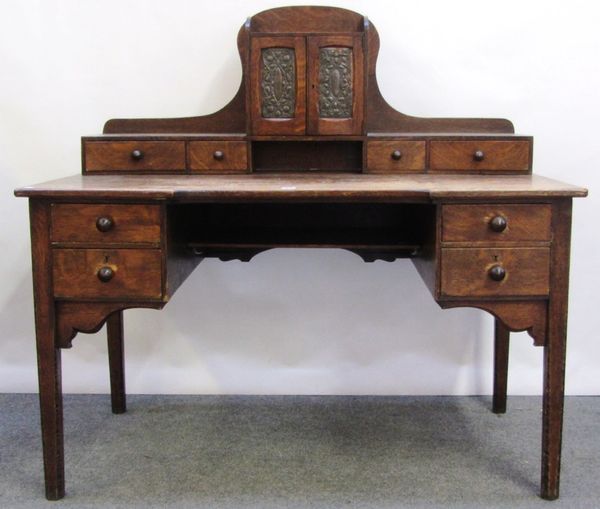 An early 20th century oak writing desk, the fitted superstructure with a pair of embossed copper doors over four frieze drawers, on tapering square su