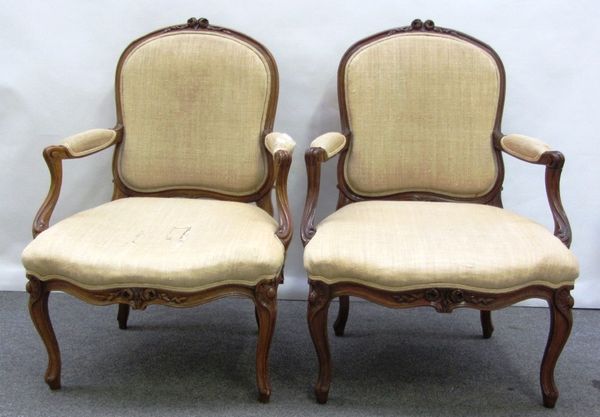 A pair of Louis XV style stained beech fauteuils, each with floral carved crest and serpentine seat, on cabriole supports.