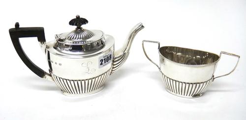 A silver teapot and a matching silver twin handled sugar bowl, each of oval form, with partly fluted decoration, the teapot with wooden fittings, Birm