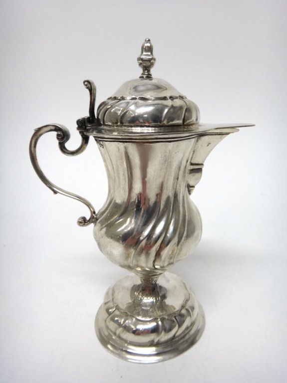 A German silver jug, from an altar cruet, of baluster form, having spiral fluted decoration and with a scrolled thumbpiece, on a circular foot, maker'