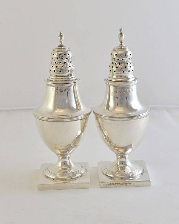 A pair of George III silver large pepper casters, each of urn shaped form, with reeded borders and raised on a square base, London 1802, height 15cm,