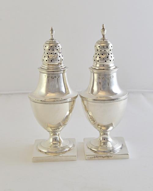A pair of George III silver large pepper casters, each of urn shaped form, with reeded borders and raised on a square base, London 1802, height 15cm,