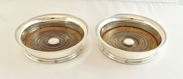 A pair of George III silver mounted bottle coasters, each of tapered circular form, with a reeded rim, turned wooden base, crest engraved to the circu