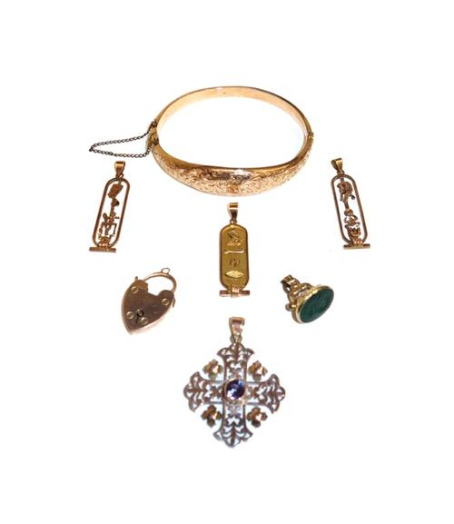 A 9ct gold oval hinged bangle, the front with feathered scroll engraved decoration, Birmingham 1911, a gold and mauve gem set pendant, in a cruciform