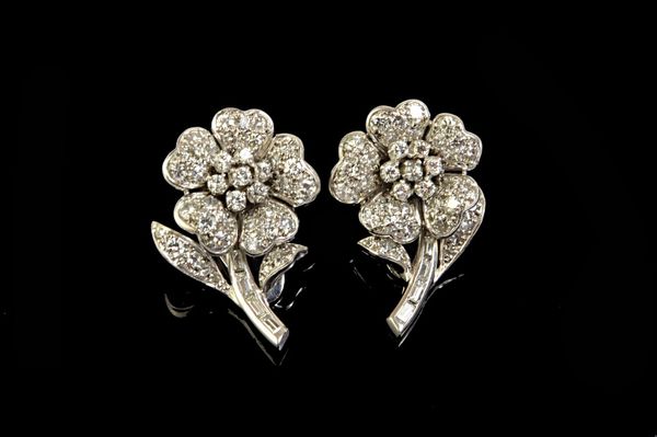 A pair of diamond set earclips, each designed as a single flowerhead spray, mounted with circular cut diamonds and with baguette diamonds mounted to t