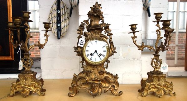 A gilt brass clock garniture, early 20th century, of 18th century French design, the clock case cast with foliate scrolls supporting a 3.5 inch white