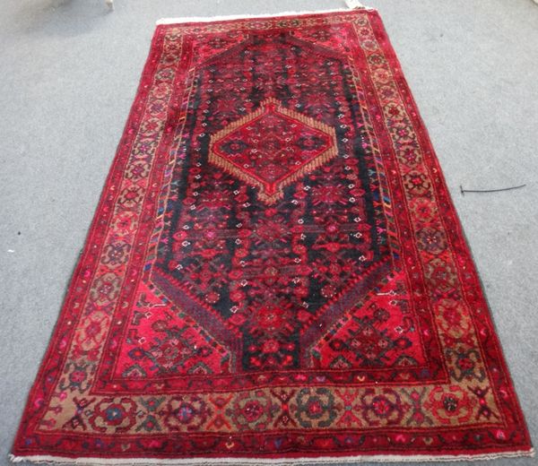 A Hamadan rug, Persian, the black field with a central madder medallion, an allover herate design, madder spandrels, a brown palemette border, 238cm x
