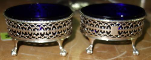A pair of George III silver framed salts, London 1772 by Robert Hennell, the scroll pierced bodies on ball and claw feet, with blue glass liners.
