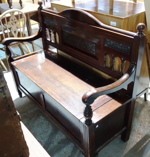 A 20th century Shoolbred style lift top settle with carved back panels.