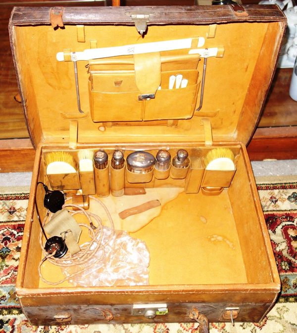 An early 20th century brown leather travelling case, with fitted interior containing silver topped bottles and faux ivory implements.