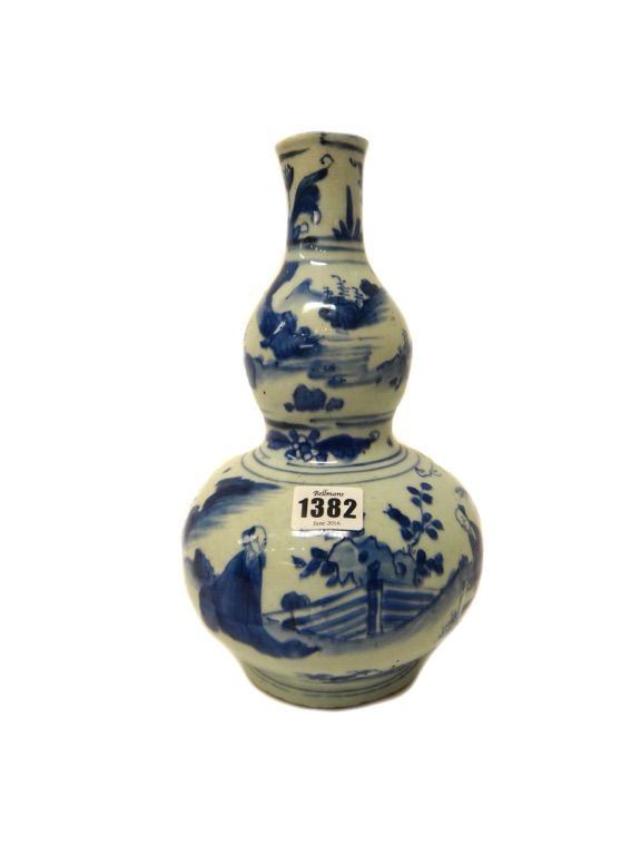 A Chinese blue and white double gourd vase, possibly mid 17th century, painted with figures in a landscape below a border of stylised tulips, 27.5cm.h