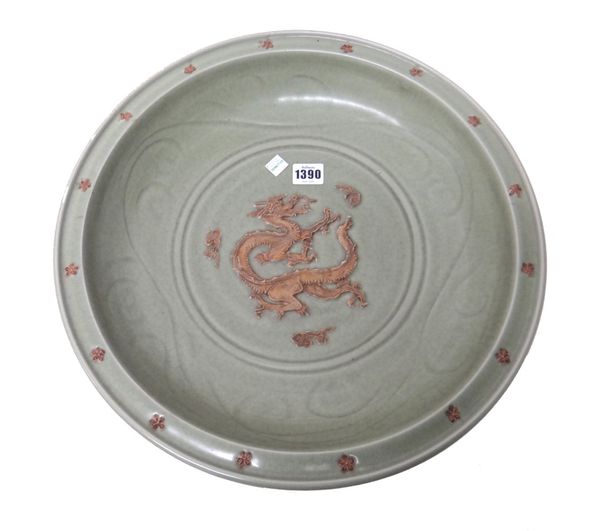 A large Chinese celadon glazed charger,the centre  moulded in relief in biscuit with a dragon chasing a flaming pearl between cloud scrolls, the well