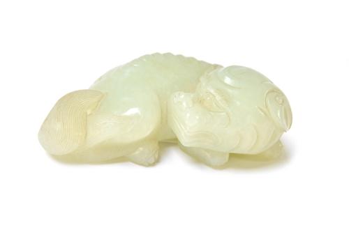 A Chinese pale celadon figure of a Buddhist lion, Qing Dynasty, 18th/19th century, carved in recumbent pose with head turned across its back, 8cm.leng