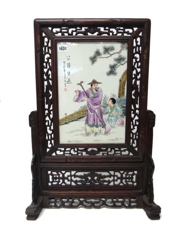 A Chinese rectangular porcelain panel, 20th century, painted with a man and boy in a fenced garden beside calligraphy, mounted in a pierced and carved