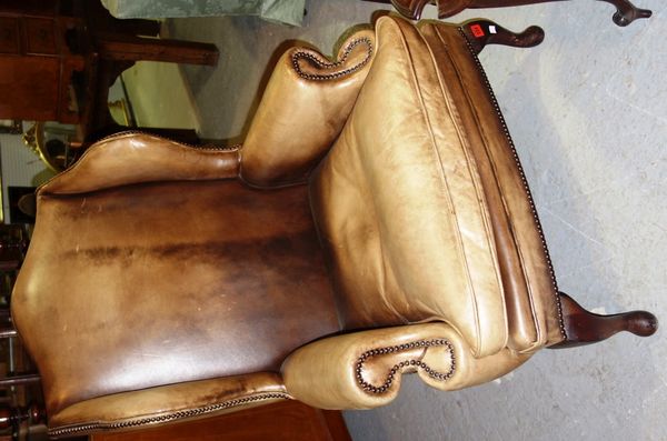 A mahogany framed brown leather upholstered wing back armchair.