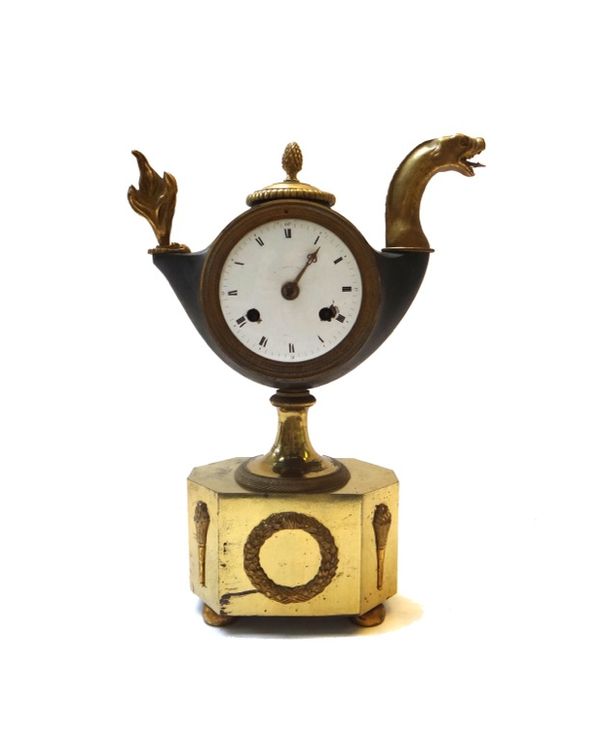 A French patinated and gilt bronze mantel clock, 19th century, the body of oil lamp form with dragon's head handle, with a white enamel dial enclosing