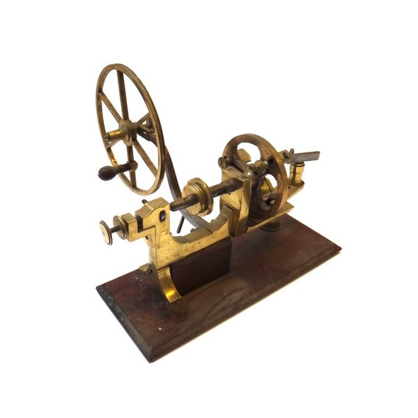 A brass watch maker's lathe, with manual fly wheel and adjustable chuck, on a mahogany base, 35cm wide.