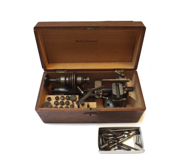 A small steel watch maker's lathe and related machined accessories, in a stained pine fitted box, 29cm wide.