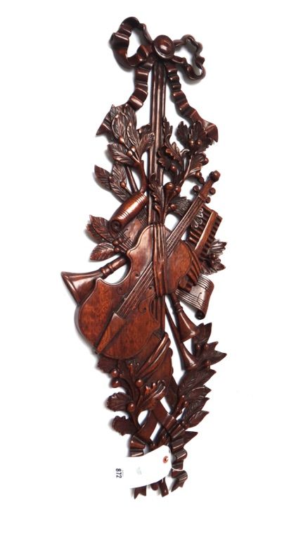 An 18th century style mahogany wall plaque, modern, carved with bow surmount over an arrangement of violins and trumpets, against a naturalistic folia