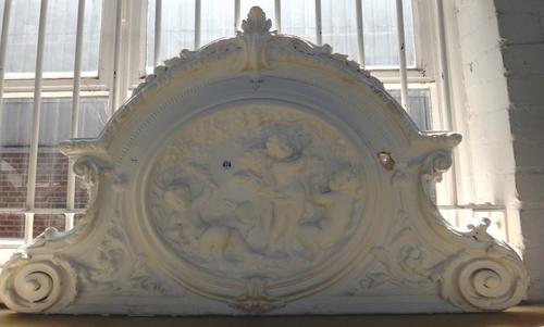 A relief moulded plaster surmount detailed with cherubic figures, 112cm wide, and a similarly decorated carved and painted wooden surmount, 120cm wide
