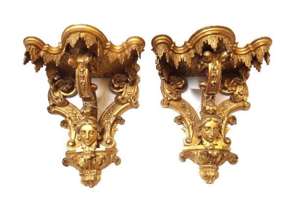 A pair of giltwood wall brackets, 19th century, the shaped top over three foliate carved stretchers centred with a female mask and acanthus carved pli