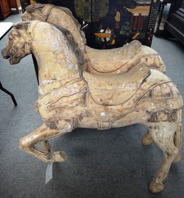 Two carved wooden fairground horses and metal footplates, each devoid of original paint, the horse 95cm high. (2)