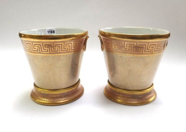 A pair of English porcelain jardinieres and stands, circa 1810, possibly Coalport, gilt with vermicule and Greek key pattern, on plain and apricot gro