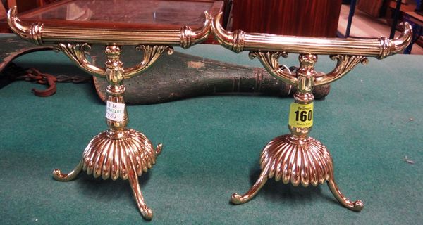A pair of late Victorian brass fire iron rests, each with reeded rest within horned ends on floral scrolling and fluted base on scroll feet, 17cms hig