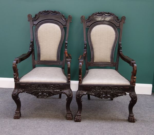 A pair of late 19th century Dutch Colonial ebony open armchairs, with carved frieze on paw feet.