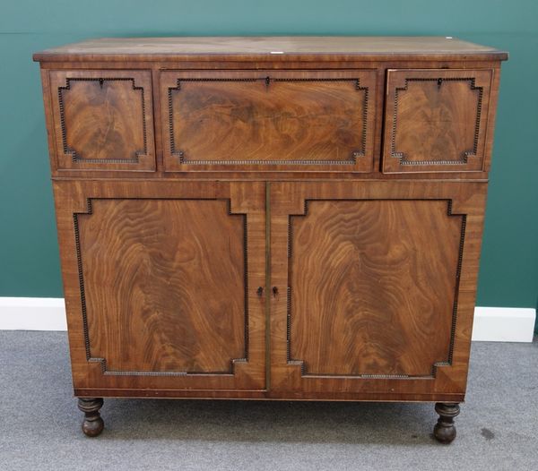 A William IV mahogany secretaire of unusual configuration, the short fitted drawer flanked by a pair of cupboards, each with pair of pull-out trays ov