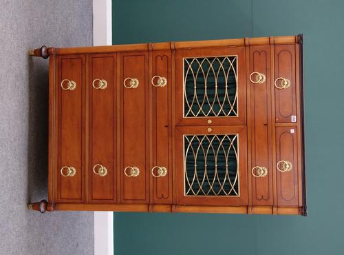 An early 20th century American satinwood side cabinet, with two short over one long drawer, over a pair of brass grille doors, enclosing three trays a