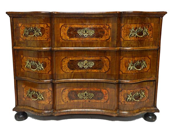 An 18th century parquetry inlaid North European commode, with shaped top and three long drawers, on bun feet, 126cm wide.  Illustrated